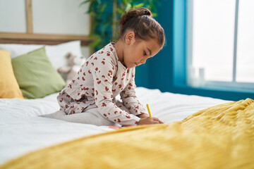 Adorable hispanic girl drawing on notebook sitting on bed at bedroom