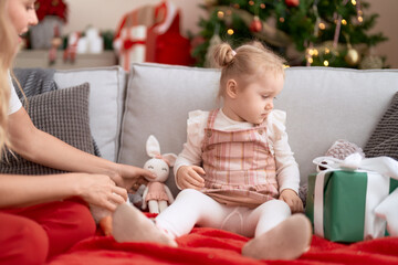Fototapeta premium Adorable caucasian girl sitting on sofa by christmas tree at home