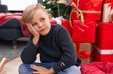 Adorable toddler sitting on floor by christmas tree with doubt expression at home