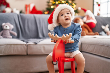 Adorable caucasian baby playing with reindeer rocking by christmas tree at home