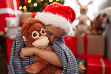 Adorable toddler hugging teddy bear standing by christmas tree at home