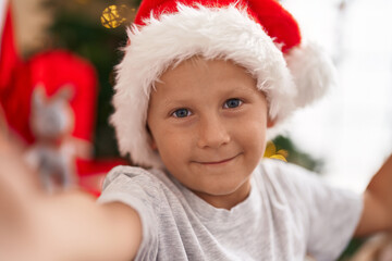 Adorable toddler make selfie by camera standing by christmas tree at home