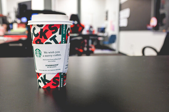 Selective focus shot of a Starbucks holiday cup on a black desk in an office