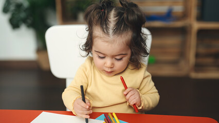 Adorable hispanic girl student sitting on table drawing on paper at kindergarten