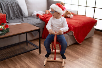 Adorable hispanic toddler wearing christmas hat playing with reindeer rocking at home