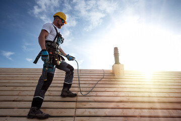 A roofer with a safety harness and tool belt standing on the roof. 
