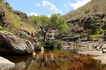 Fototapeta na wymiar Small valley with a stream of calm waters, between rocks and vegetation. Region of Conceiçao de Mato Dentro in Minas Gerais, Brazil