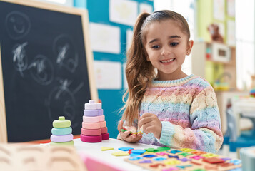 Adorable hispanic girl playing with maths puzzle game standing at kindergarten