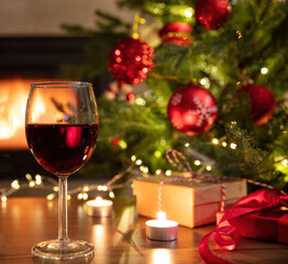 Christmas celebration. Red wine glass, Xmas presents and decoration on table, fireplace background. Xmas celebration