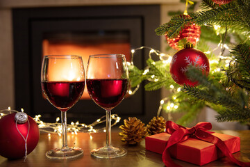 Christmas celebration. Red wine glasses, Xmas presents and decoration on table, fireplace background. Xmas celebration