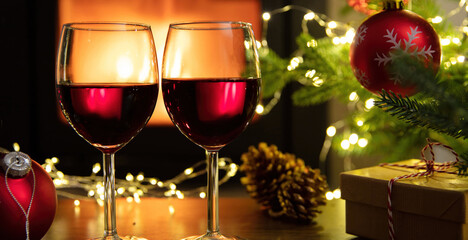 Christmas celebration. Red wine glasses, Xmas presents and decoration on table, fireplace background. Xmas celebration
