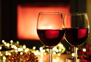 Christmas celebration. Red wine glasses and decoration on table, fireplace background. Xmas celebration