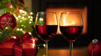 Christmas celebration. Red wine glasses, Xmas presents and decoration on table, fireplace background. Xmas celebration