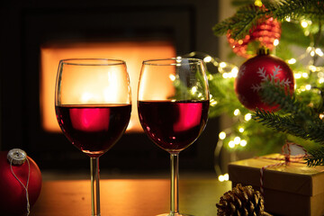 Christmas celebration. Red wine glasses, Xmas presents and decoration on table, fireplace background. Xmas celebration
