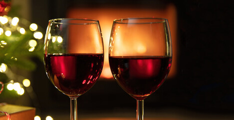 Two red wine glasses and bokeh lights decoration on burning fireplace background,