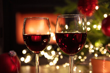 Christmas celebration. Red wine glasses, Xmas presents and decoration on table, fireplace background. Xmas celebration