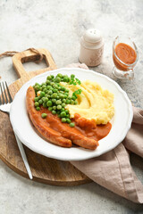 Bangers and mash. Grilled sausages with mash potato and green pea on white plate on grey background. Traditional dish of Great Britain and Ireland. BBQ beef sausages. Top view.