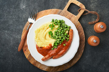 Bangers and mash. Grilled sausages with mash potato and green pea on white plate on black dark  background. Traditional dish of Great Britain and Ireland. BBQ beef sausages. Top view.
