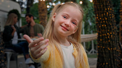 Portrait cute little child outdoors camping small kid girl baby schoolgirl daughter waving hand inviting welcome gesture come here invite Caucasian parents mom and dad near van talking on background - obrazy, fototapety, plakaty