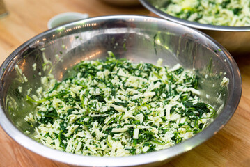 A bowl of grated cheese mixed with chopped herbs. The filling for the cheese pie.