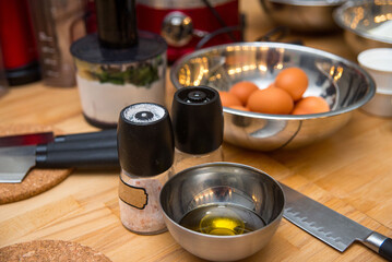 kitchen table with ingredients and utensils before cooking. bowl with oil, knives, mill with salt and pepper.