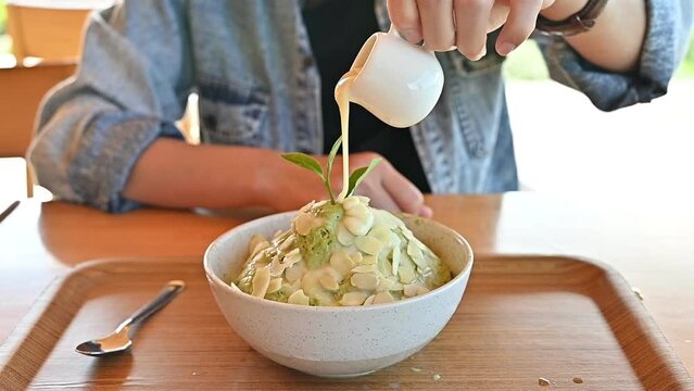 Someone pouring condensed milk on Matcha Bingsu before eating. Bingsu is a traditional dessert in Korea.