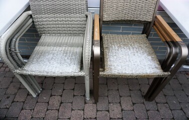 Schneebedeckte braungraue Baststühle vor Restaurant am Mittag im Winter