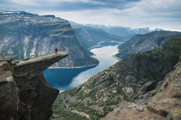 Obraz na płótnie Canvas A person standing on the reef called trolltunga looking at the breathtaking view on norway lake and mountains. Norway famous place. Summer hiking. 