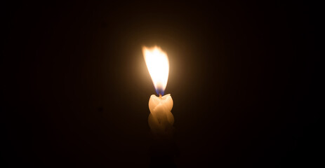 A single burning candle flame or light glowing on a spiral white candle against little blowing wind on black or dark background on table in church for Christmas, funeral or memorial service