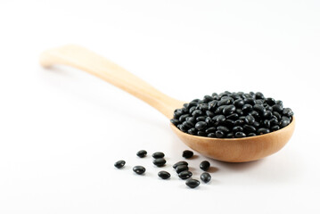 Black beans in a wooden ladle and placed on a white floor, selective focus.