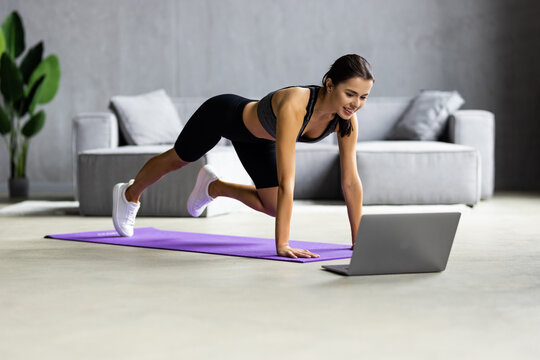Fit woman doing yoga plank and watching online tutorials on laptop training in living room - Image o