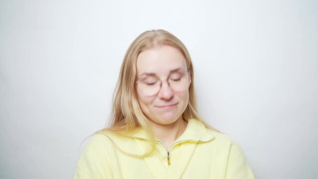 European young beautiful blonde woman in glasses nods head to indicate agreement, and then disagree. Woman smiling, says yes, then no, then so-so reaction, middling. White background stock video