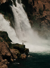 Man fishing next to the waterfall. Small people big world concept. People and nature concept. 