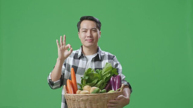Asian Male Farmer With Vegetable Basket Showing Ok Gesture And Smiling While Standing In The Green Screen Studio
