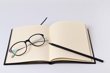 Eyeglasses on a notebook with a pencil on a white background, selective focus, poor vision concept