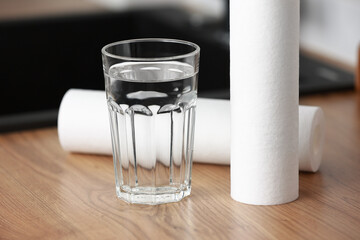 A glass of clean water and foamed polypropylene filter cartridges on wooden table in a kitchen...