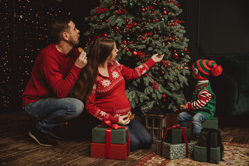 Happy family under Christmas tree. baby boy in Santa Claus hat with gifts under Christmas tree with many gift boxes presents. Happy Holidays, New year. Cozy warm winter evening at home. Xmas time