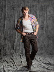 A relaxed dude in a colorful shirt and a white T-shirt, posing in the studio on a gray background