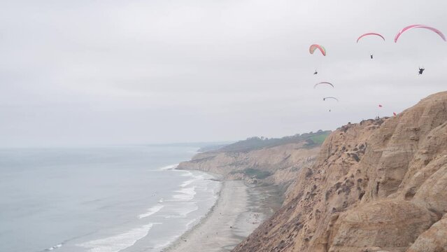 People paragliding, Torrey Pines cliff or bluff. Paraglider soaring in sky air, flying on parachute, kite or wing. Recreational sport hobby. Ocean coast, San Diego, California USA. Para gliding flight