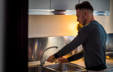 Attractive young man using tap water from kitchen sink
