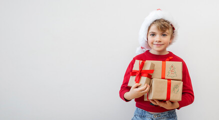 Excited funny Canadian caucasian child girl boy wear red Santa hat holding Christmas gift boxes dreaming over white background. Copy space. Merry Christmas presents shopping sale.