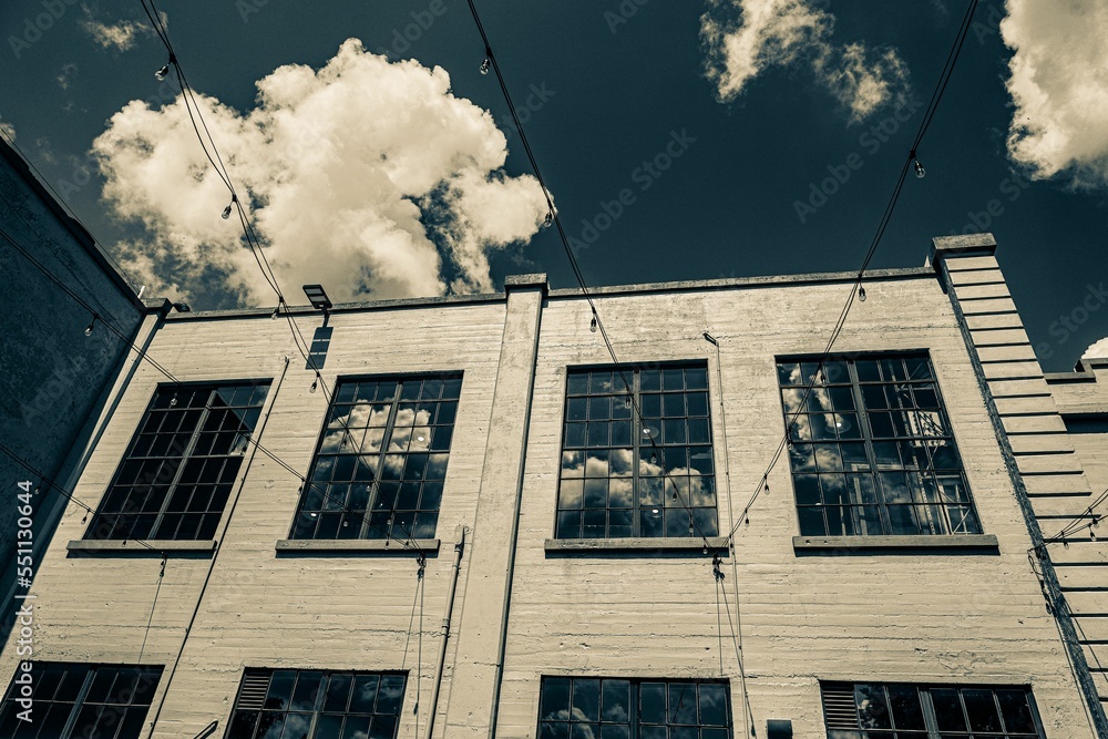 Poster low angle of a large brick industrial building with clouds and sky reflecting in windows