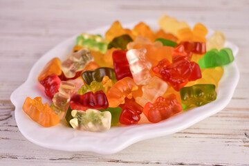 Lots of multi-colored jelly bears on a white plate. Close-up.
