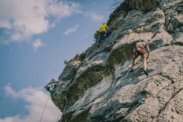 Male and female rock climbers with the lead that secures the partner, three people climbing on the rocks.