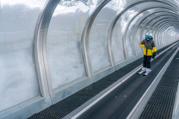 A boy on skis stands on a magicagic carpet ski lift in a glass tunel. Snowy winter day in the...