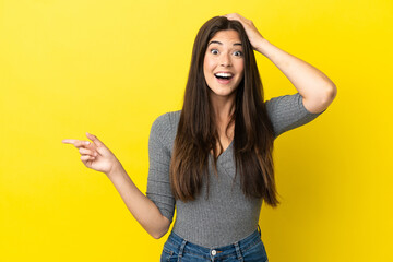 Young Brazilian woman isolated on yellow background surprised and pointing finger to the side