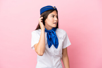 Airplane stewardess Brazilian woman isolated on pink background listening to something by putting hand on the ear