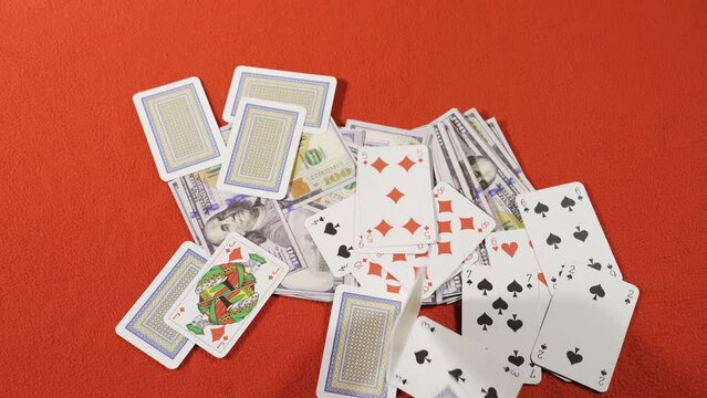 Playing cards falling on the dollar at the gambling table. Gambling and betting.
Playing cards falling on a stack of dollars on a red gambling table.
