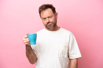 Middle age caucasian man holding cup of coffee isolated on pink background with sad expression