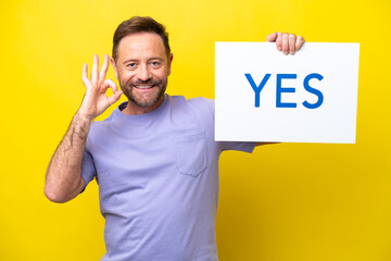 Middle age caucasian man isolated on yellow background holding a placard with text YES